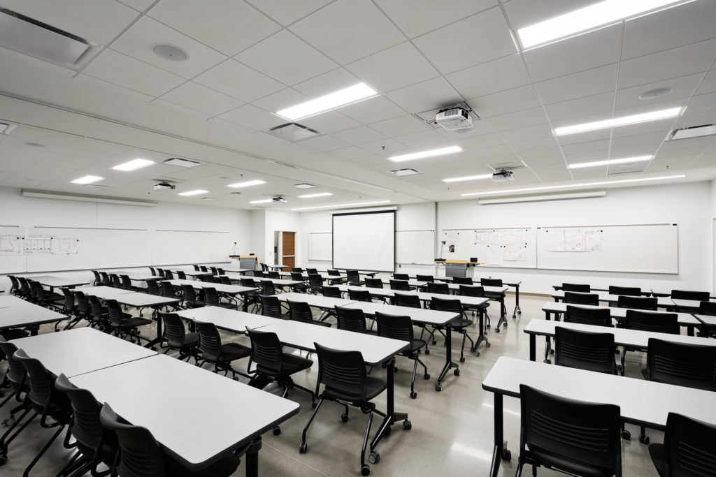 An empty classroom, lights on and every seat free.